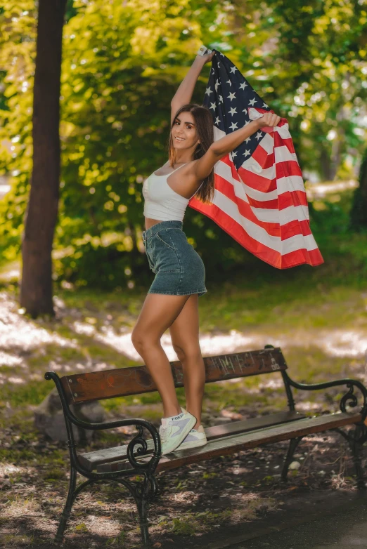 a beautiful woman holding a flag stands on a bench