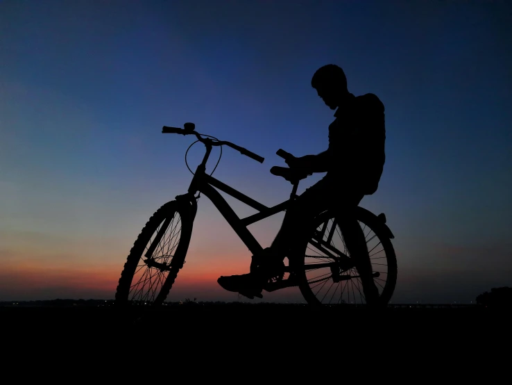 a man standing with a bike against a purple and blue sky