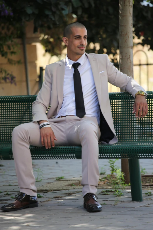 a balding man in a gray suit and black tie sitting on a green bench