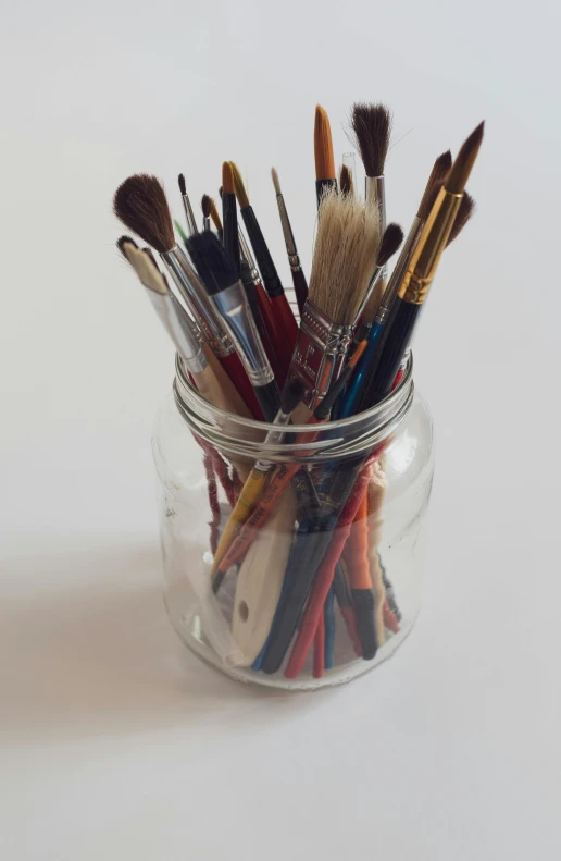 a jar filled with various paints and brushes