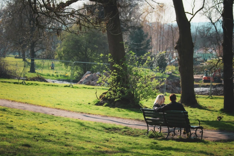 two people sitting on a bench next to trees