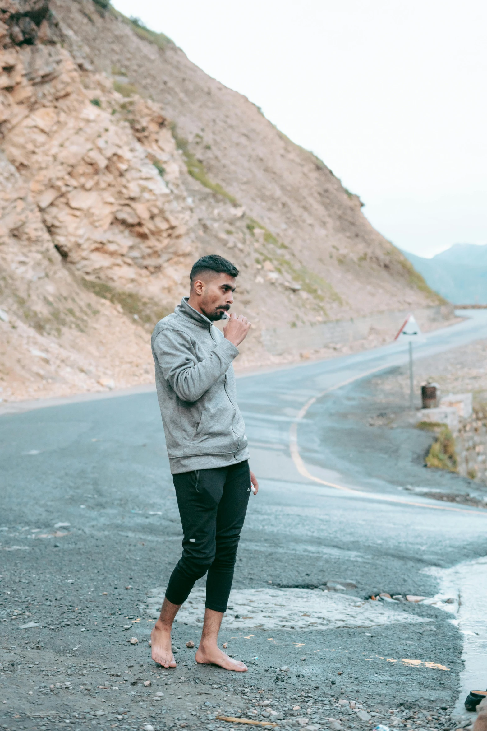 a man with a surprised look standing on a road near a mountain