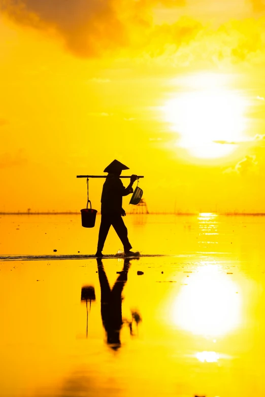 the man with the umbrella and hat is walking in the water at sunset