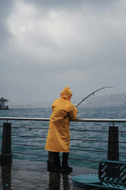 a person in a yellow rain coat on the pier with a fishing rod