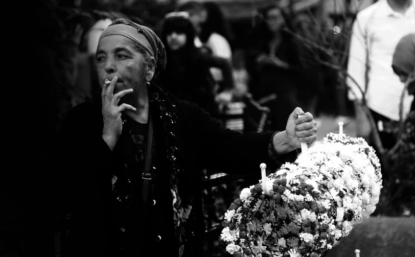 an older woman smokes a cigarette near flowers
