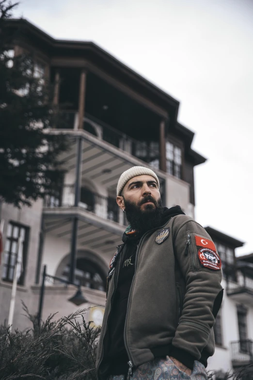 a man with a beard and a beanie in front of a building