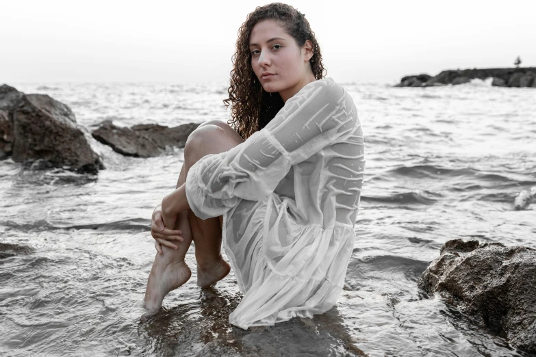 a woman sitting on some rocks in the water