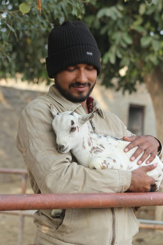 a man holds a baby goat next to a railing