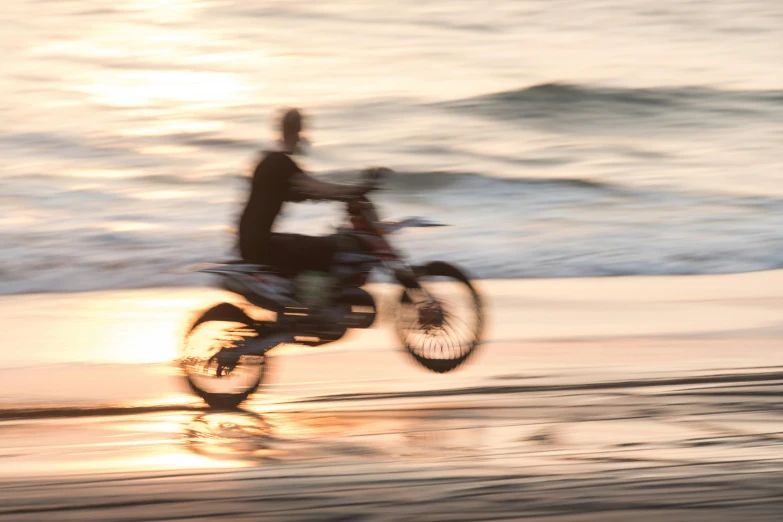 a blurry po of the back end of a man riding a dirt bike on a beach