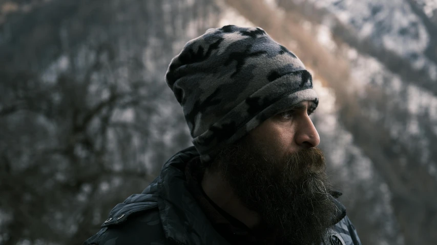 bearded man in a winter hat looks off into the distance