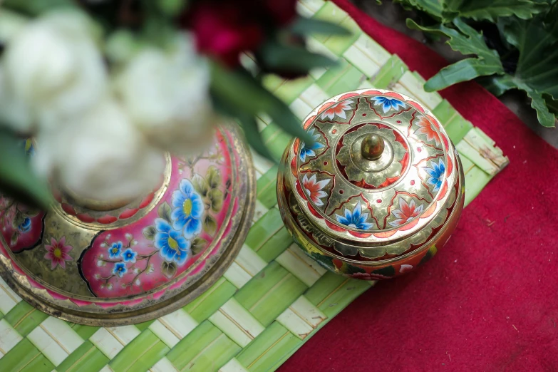 a gold box with flower designs sits in front of an ornate vase