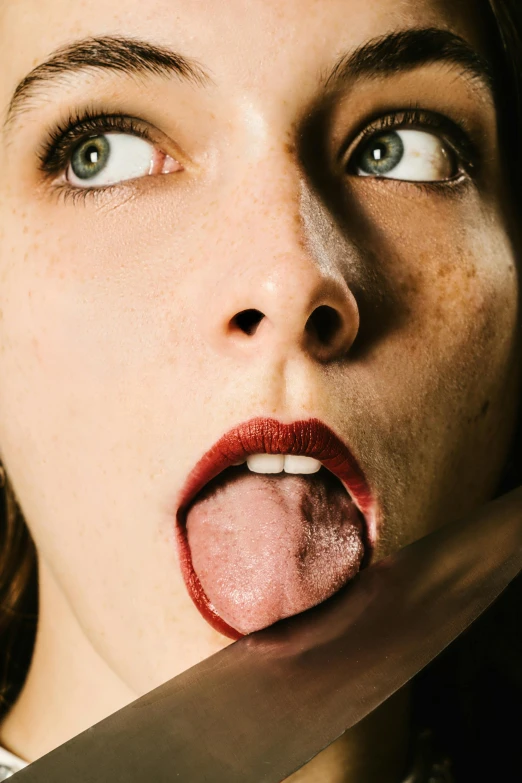 a woman sticking her tongue out as she holds a large knife up to her face