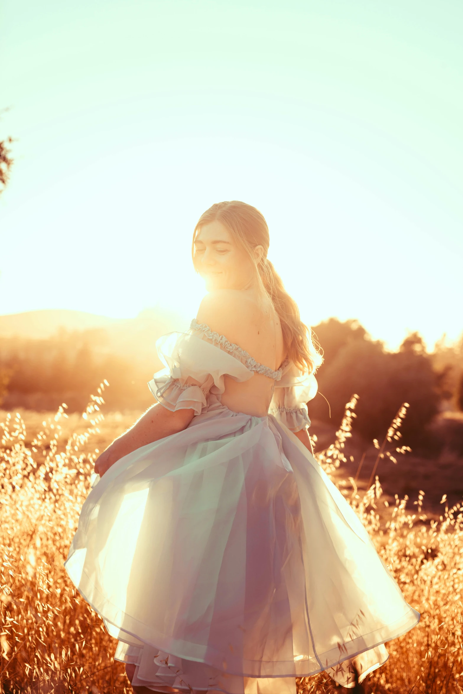  standing in field at sunset in long dress