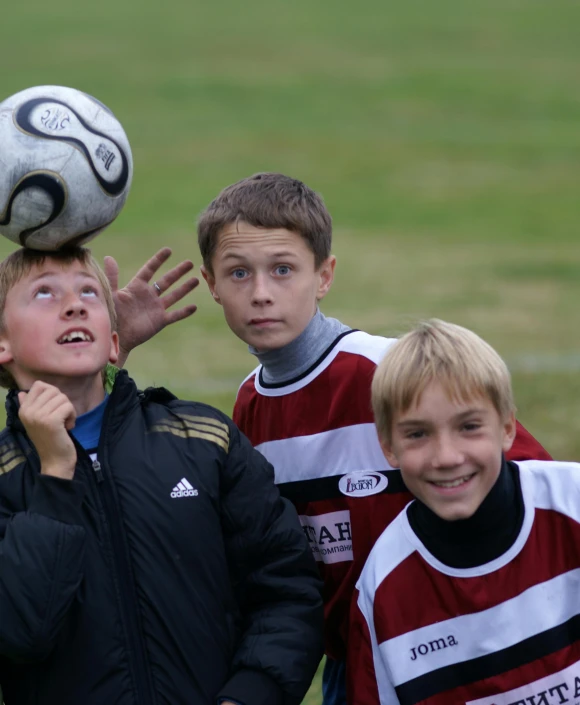 three boys playing soccer while wearing matching jackets