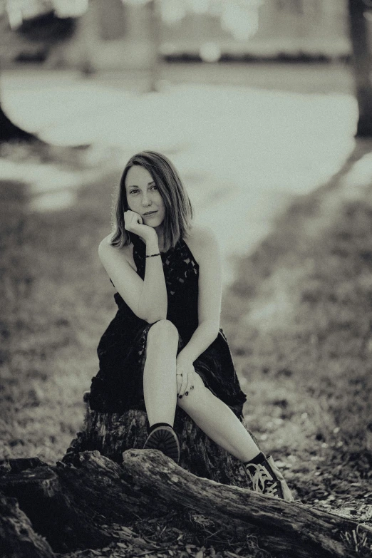 a woman in the woods looking down while sitting on a log