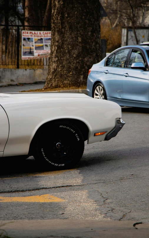 a white car and silver car sit parked next to each other on the street