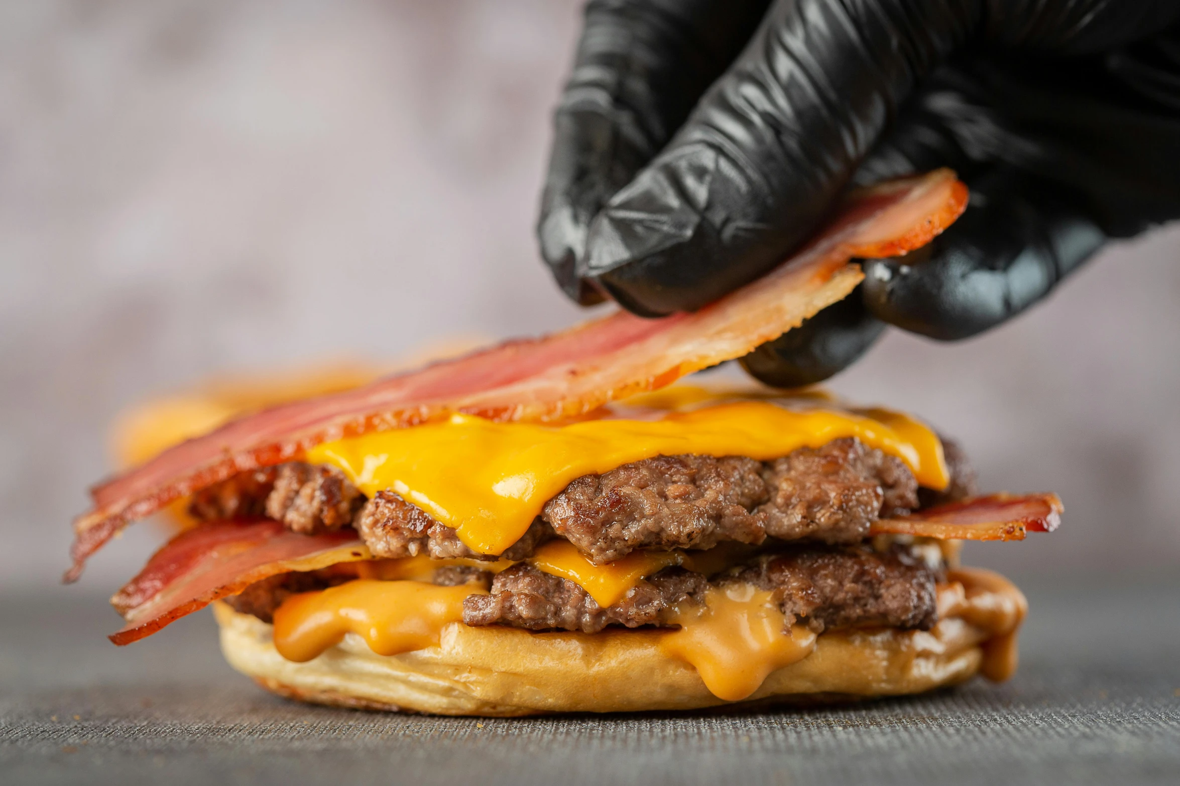 there is a hand that is grabbing some bacon from a cheeseburger