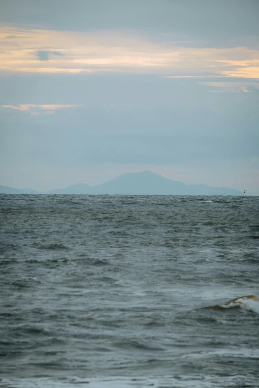 the sky and ocean is overcast and a distant hill