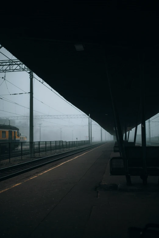 a yellow train is going under a overhang at an empty train station