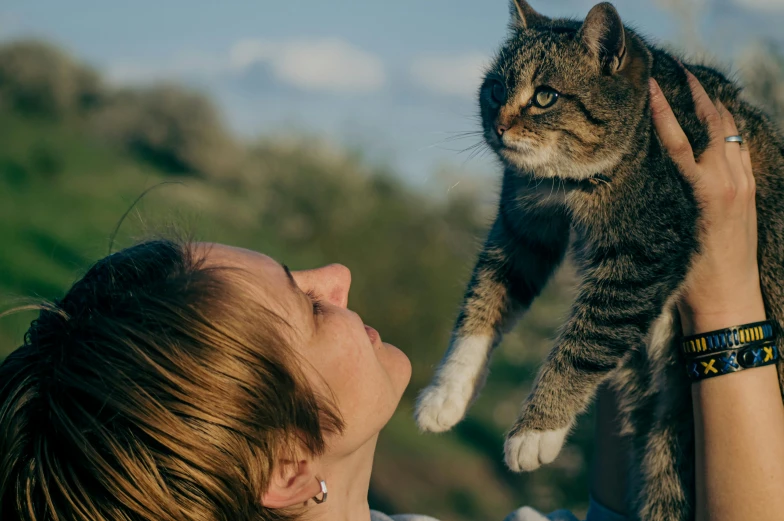 a woman holding up a cat with her face close to her mouth