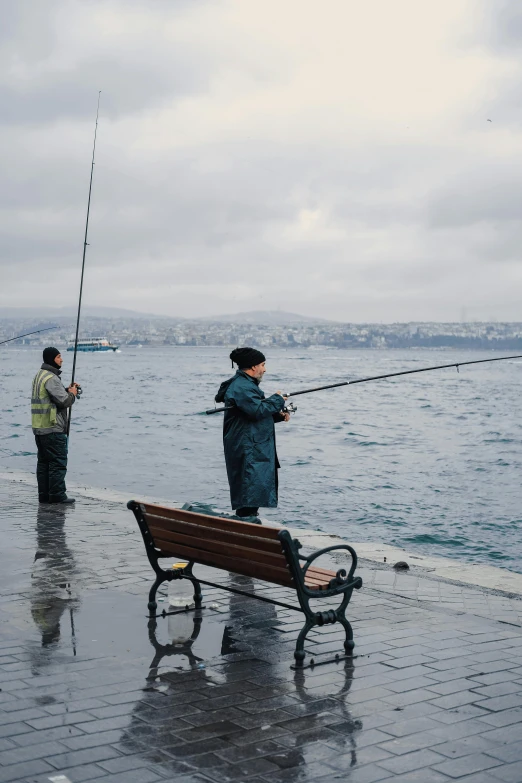 two men with fishing poles standing on a beach near the water