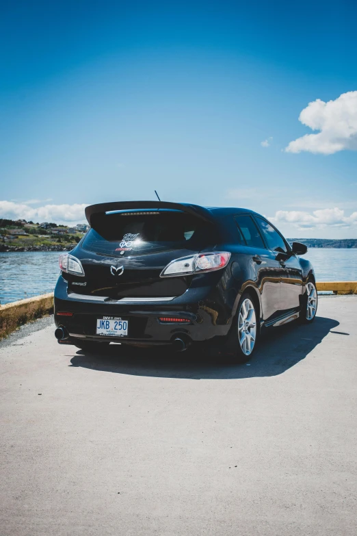 a black car parked by the water and some clouds