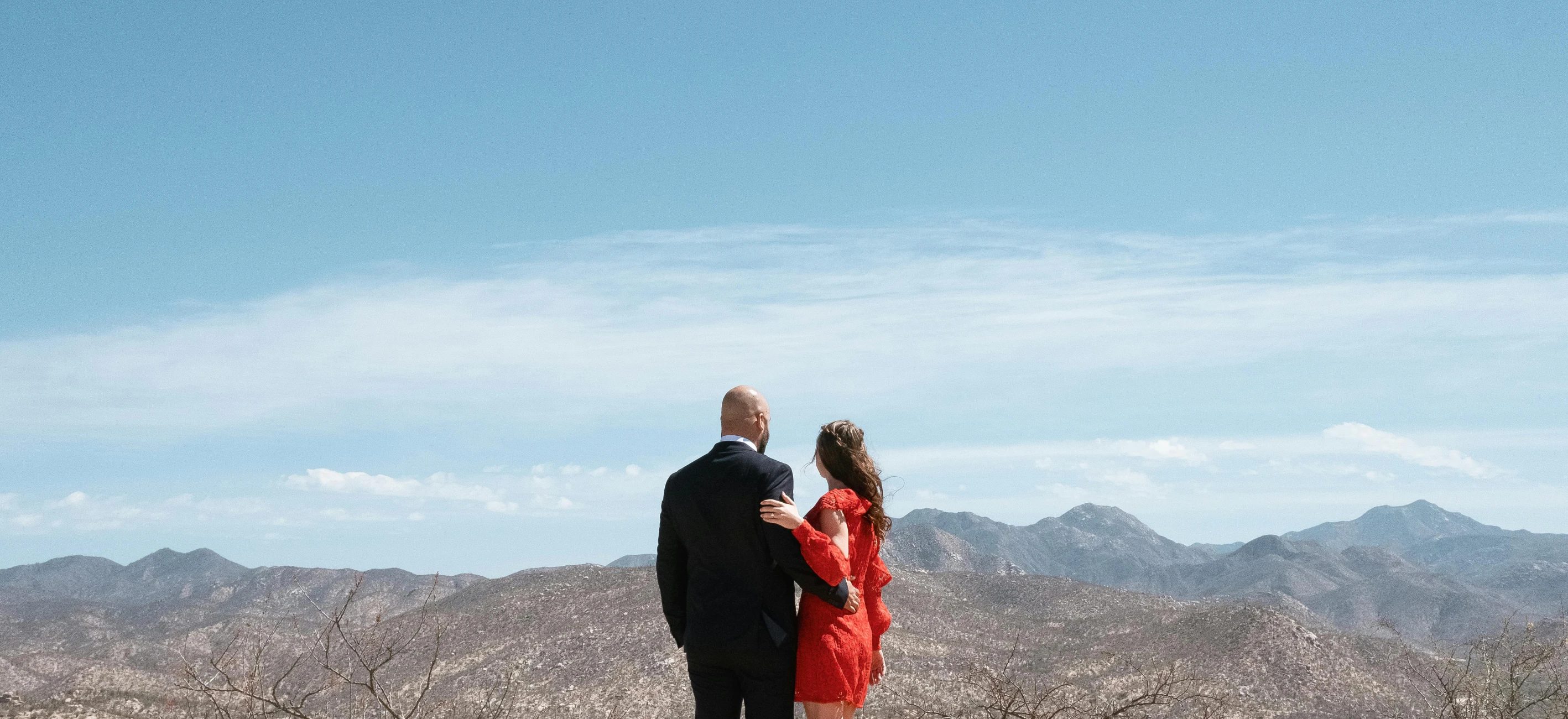 a man and woman standing on top of a hill with their backs to the camera