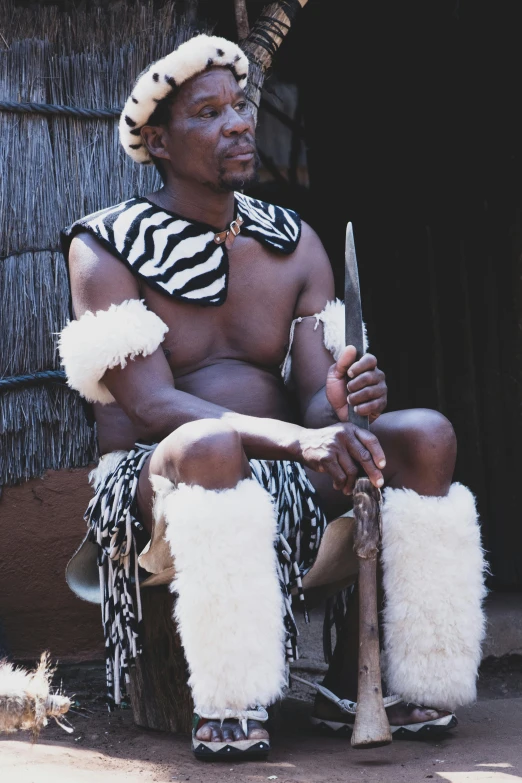 a man with white hair and animal skin sits on the ground next to two knives