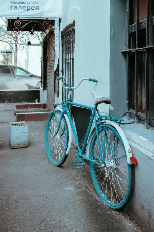 a blue bicycle sitting against a building near the sidewalk