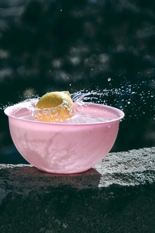 a lemon is falling into a pink bowl