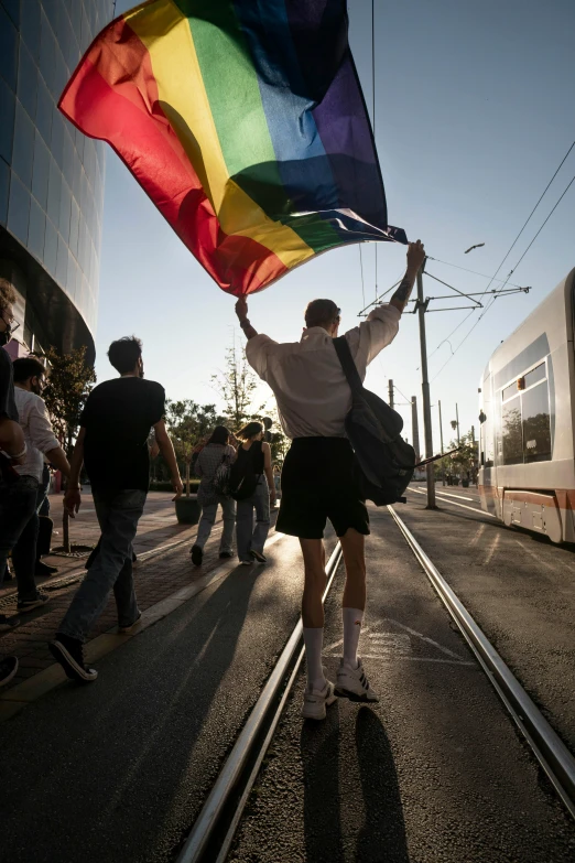 woman holding up a colorful flag while standing in a street