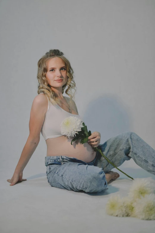 a pregnant woman sitting on the ground with flowers in her lap