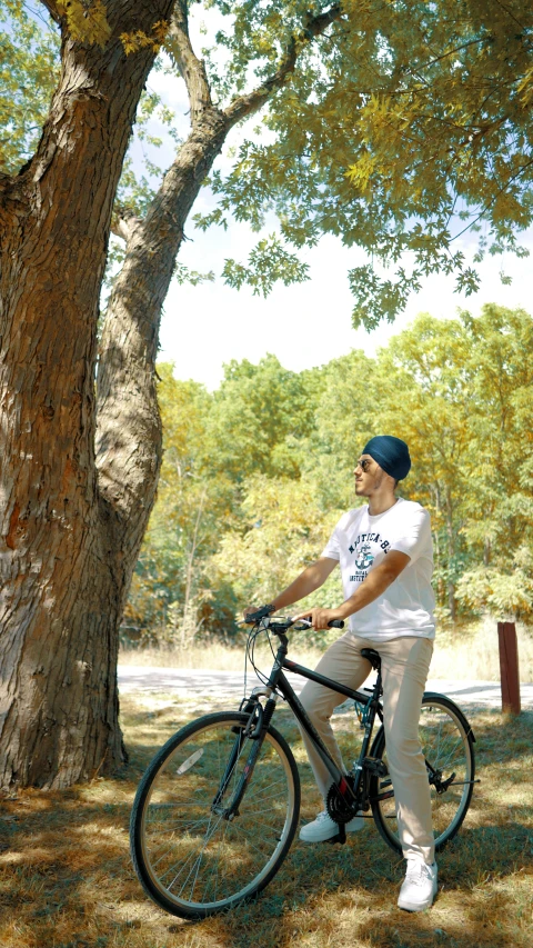 a man wearing a hat sits on top of a bike next to a tree