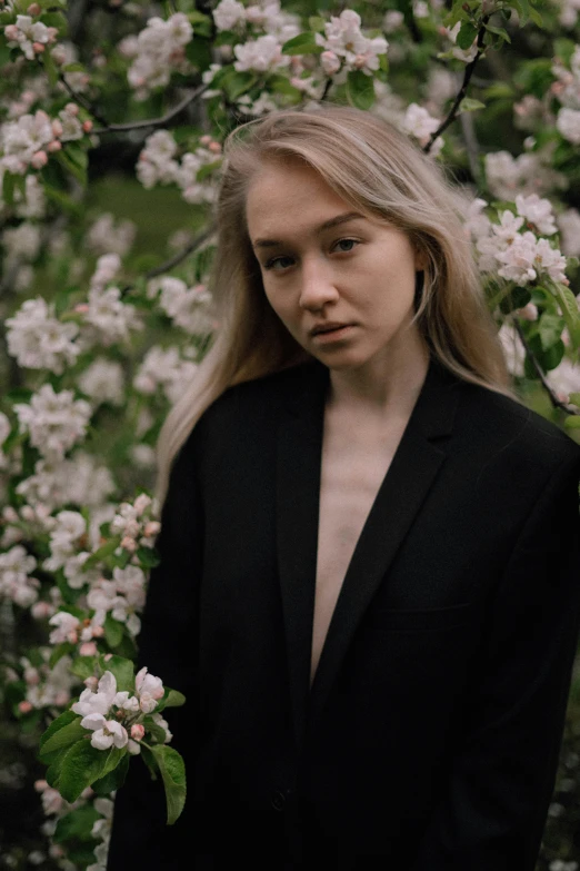 a woman in black jacket standing under a tree filled with flowers