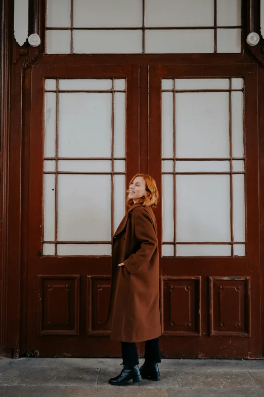 the girl stands in front of the brown door of an old building