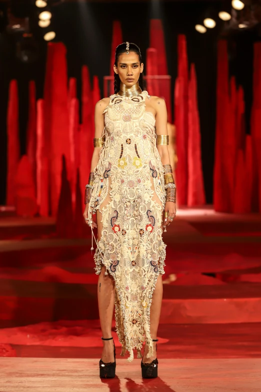 a woman walks down the runway in an ornate frock