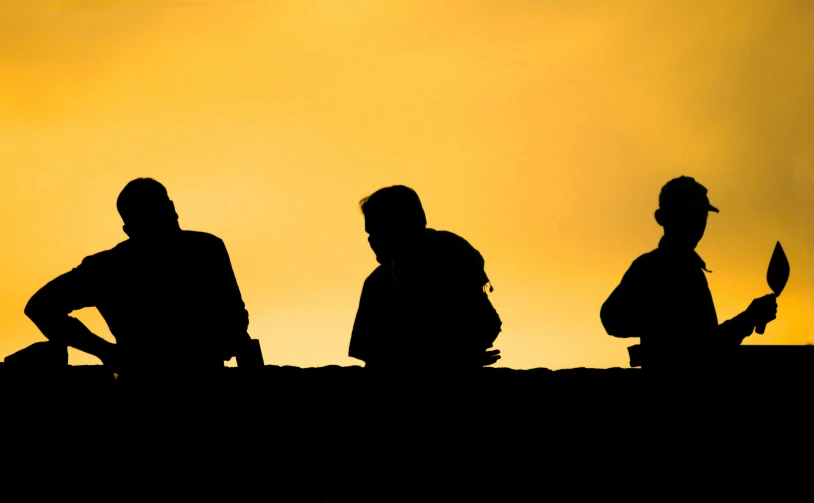 the silhouette of three people are sitting against an orange and yellow sky