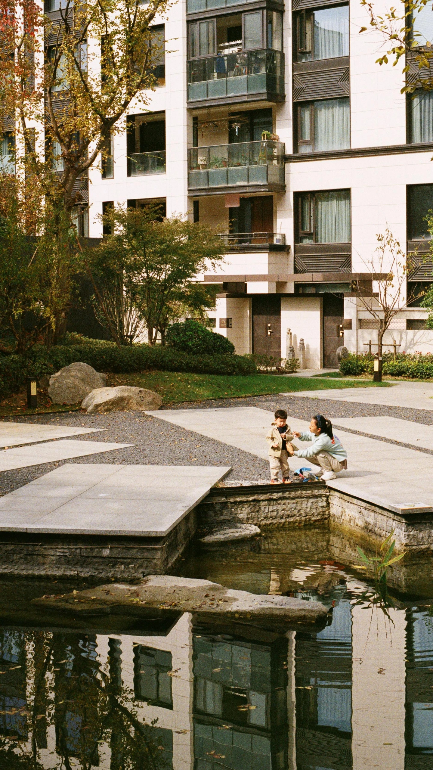 two people sitting on the ledge of a pond