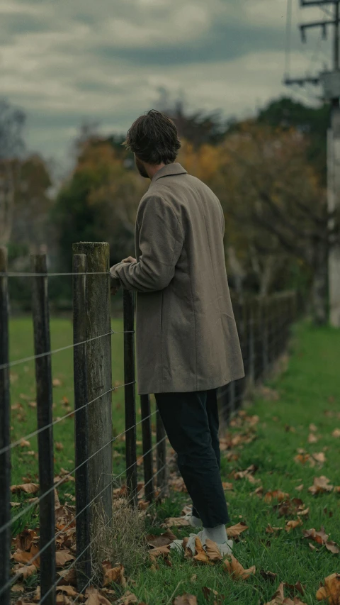 a man leaning on a fence in the grass