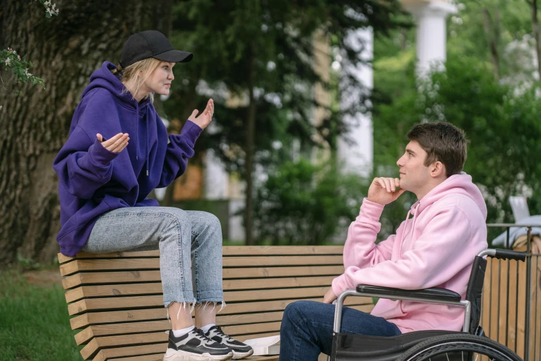 the man in pink jacket and woman seated on a bench talking to each other