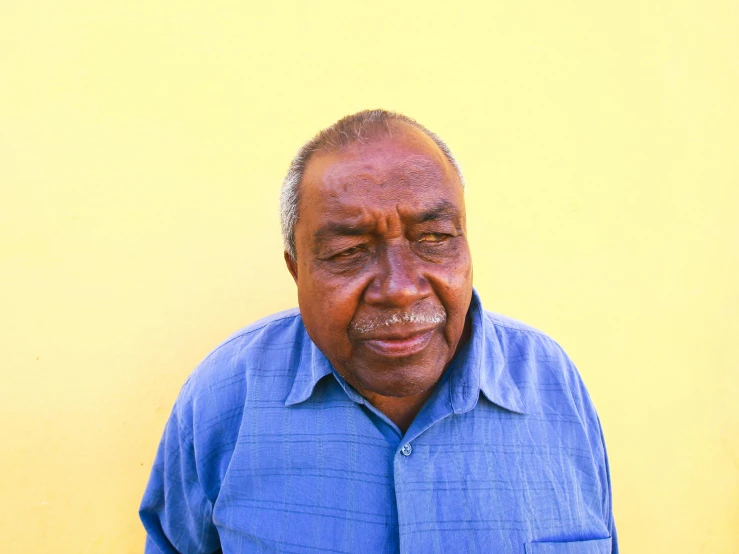 an older man stands against a yellow wall