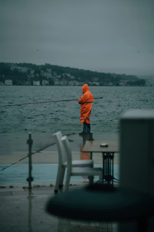 an orange jacketed man standing on the edge of the water holding onto some ropes