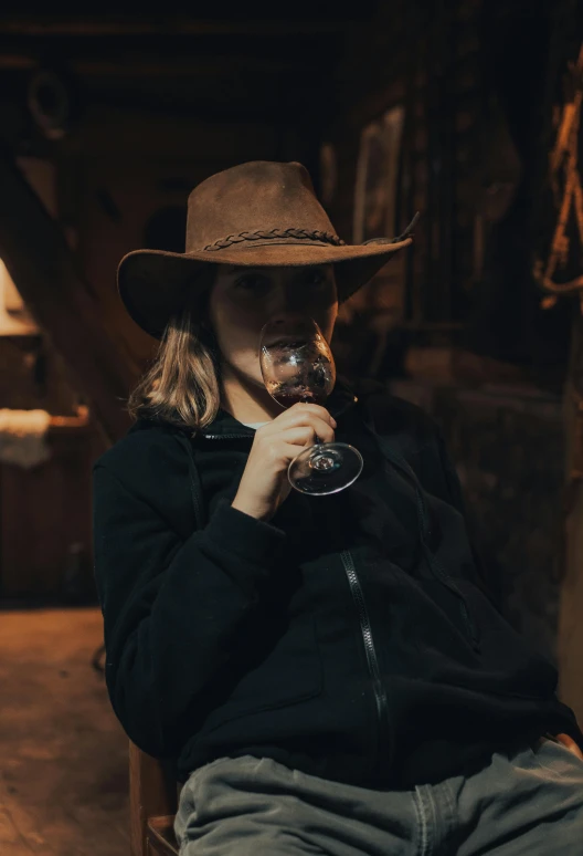 a young woman sits in an old barn drinking from a wine glass