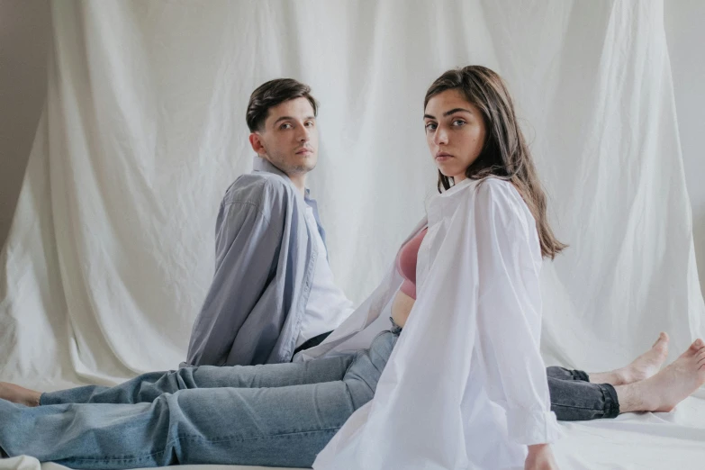 a couple in white shirts and jeans sit on the floor