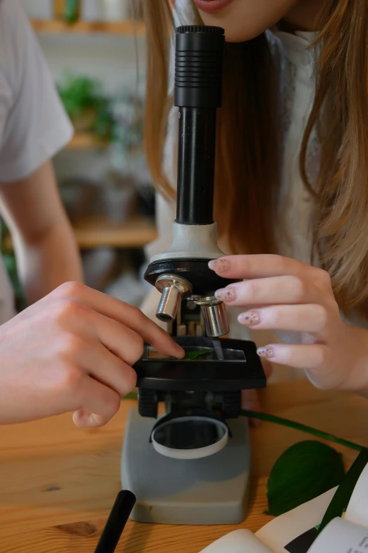 a girl looking through a microscope while another girl looks on