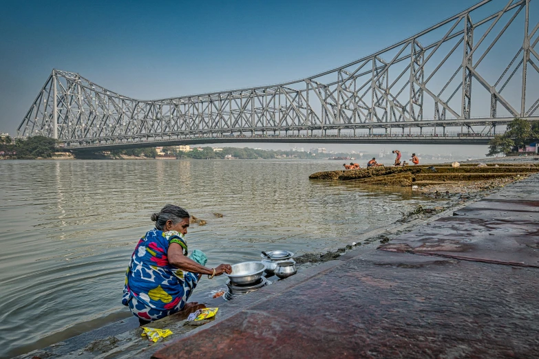 an indian woman is cooking on the dock in front of a large bridge