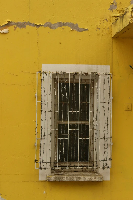 a window in a yellow wall with black bars on it