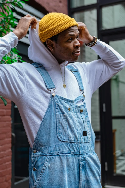 a man wearing overalls and a knitted hat, standing outside