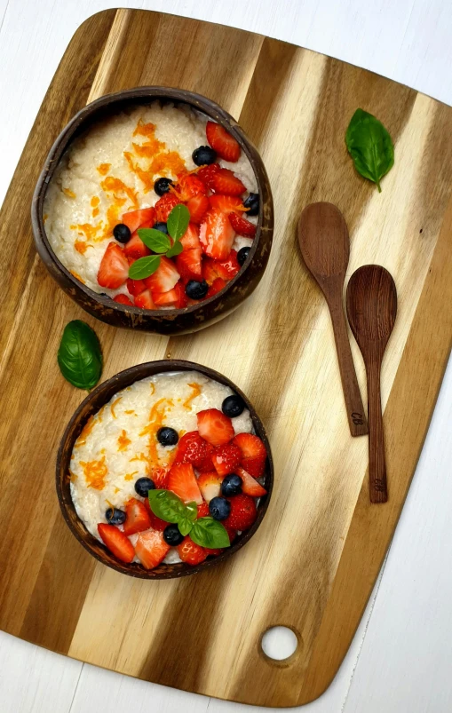 two bowls of cereal and fresh fruit served on  board with a spoon