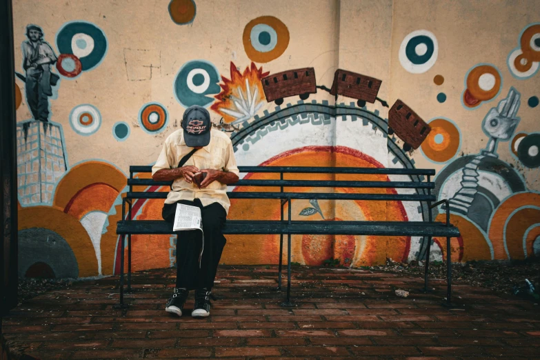 an old man sitting on a bench in front of a painted wall